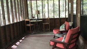 Une véranda couverte avec un plancher en bois, une table avec des chaises et un ventilateur de plafond.