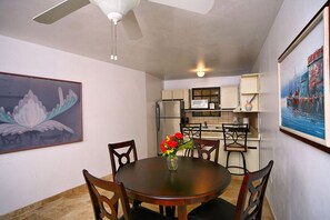 A dining area with a round table, chairs, a vase with flowers, a ceiling fan, and kitchen cabinets in the background.