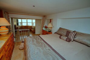 A bedroom with a large bed, a dresser, a lamp, and a view of a balcony.