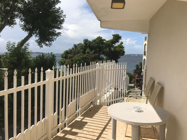 A balcony with a white fence, a round table, and chairs, overlooking a body of water and trees.