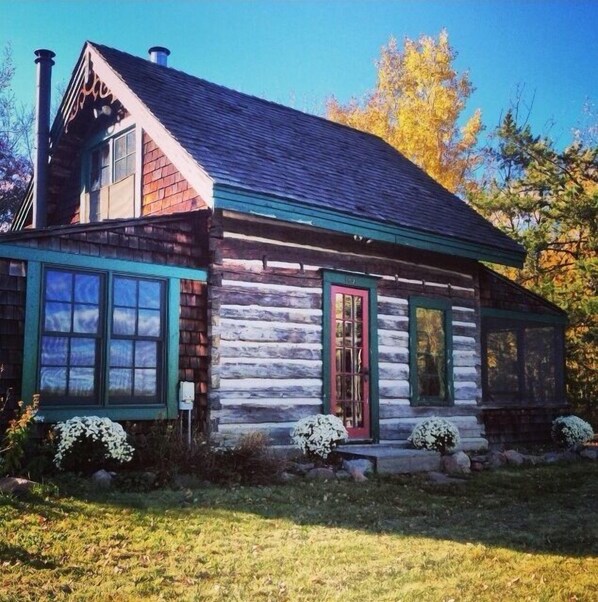 Cozy cabin with a front porch, chimney, and green-framed windows.