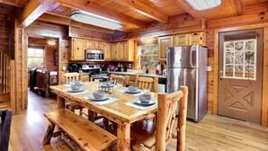 Une cabane en bois comprenant un coin repas, une cuisine et une grande porte dotée d’une fenêtre.