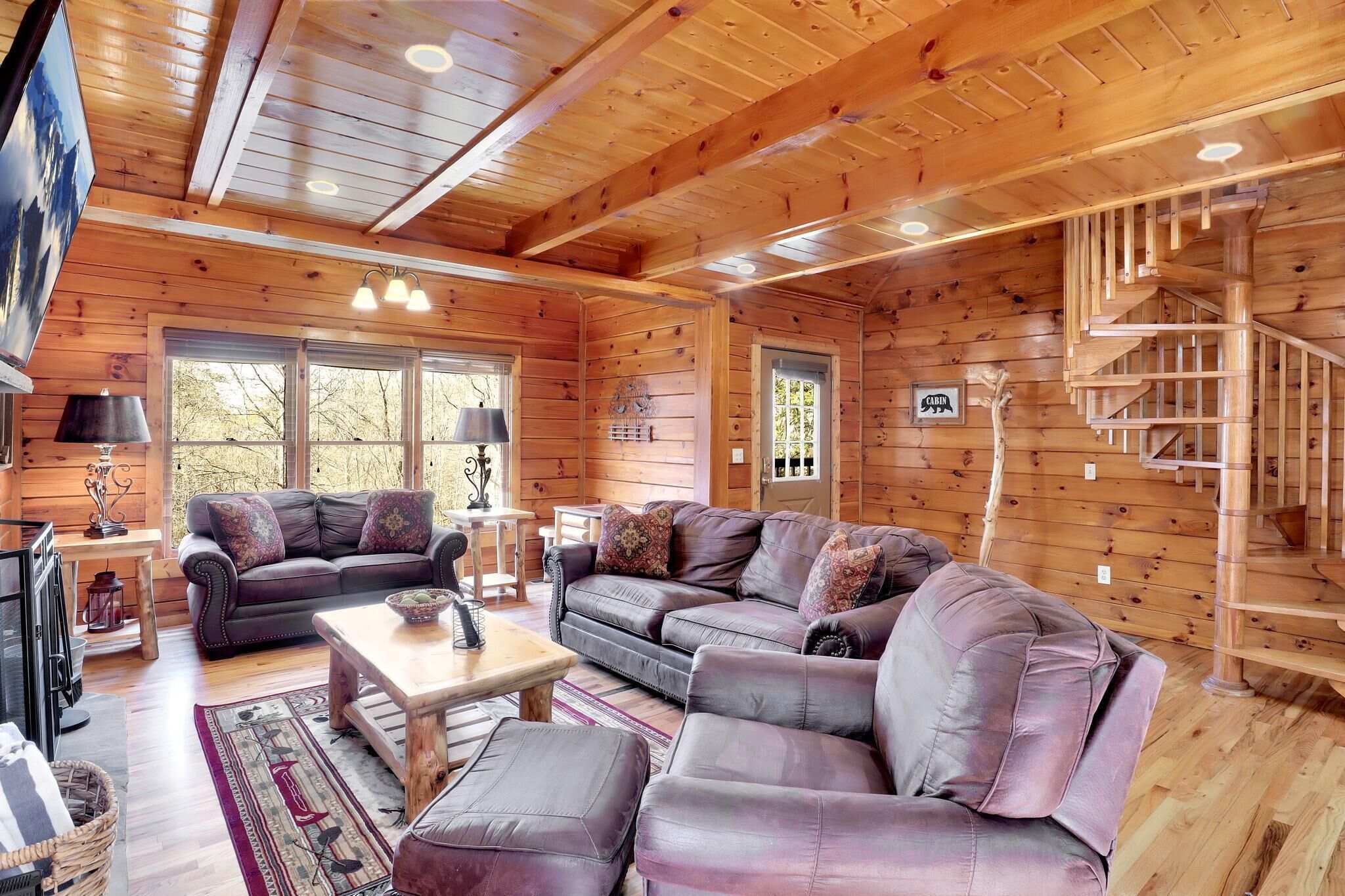 A log cabin interior with a wooden staircase, leather sofas, and a dining area.