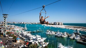 A cable car system over a marina with boats and buildings in the background.
