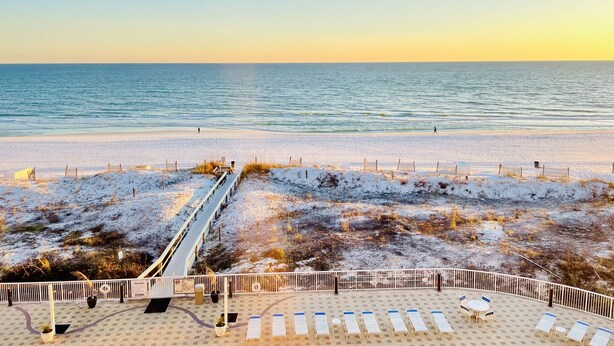A beach with a walkway leading to the water, sun loungers, and a fenced area with a view of the ocean.
