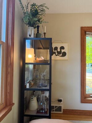 Una habitación con una estantería de madera que contiene diferentes vasos y una planta en maceta.