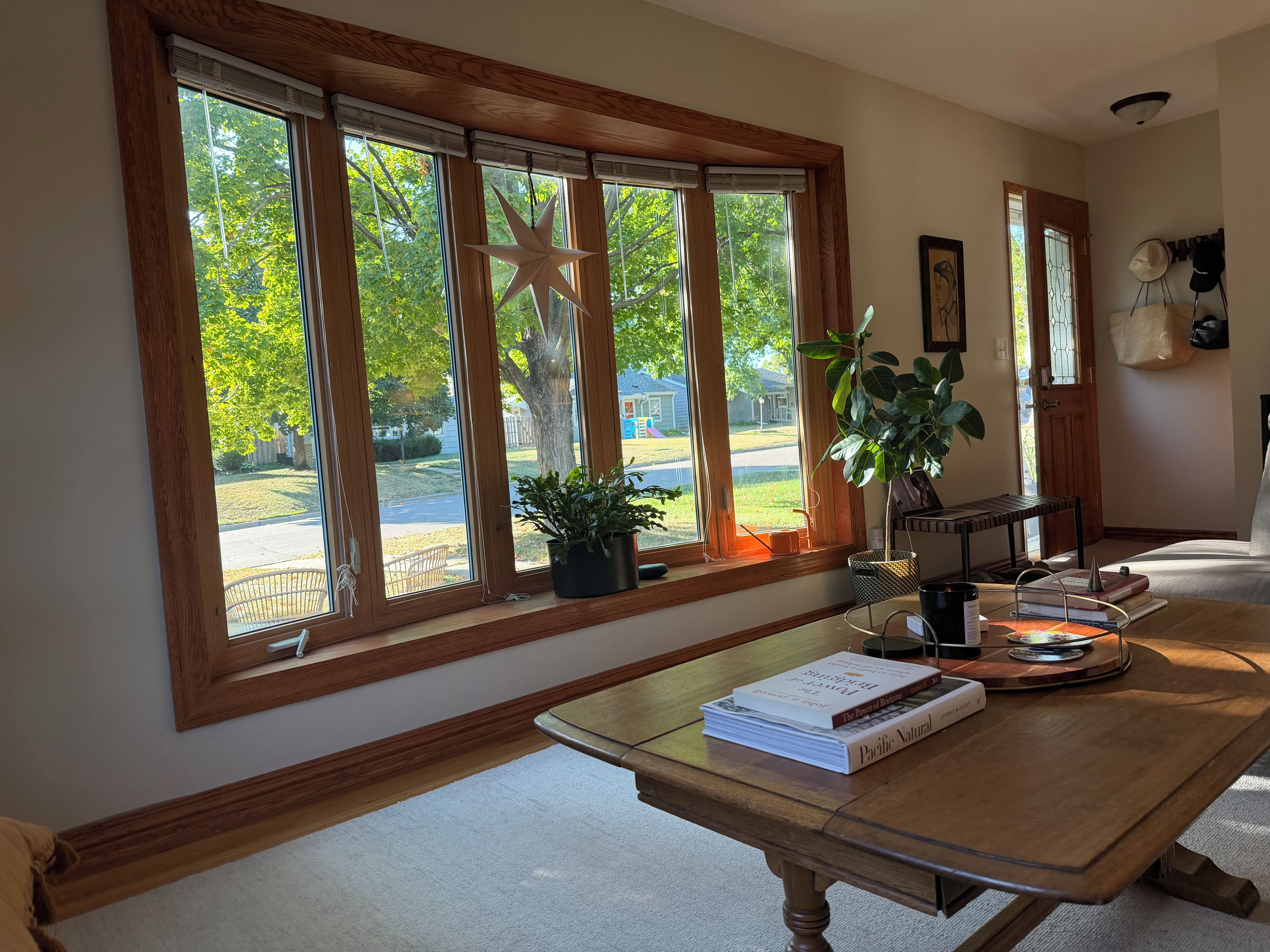 A room with large windows, a wooden table with books, a star decoration, and a plant.