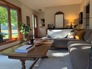 Una sala de estar con sofá, mesa de centro y vistas al exterior a través de amplios ventanales.