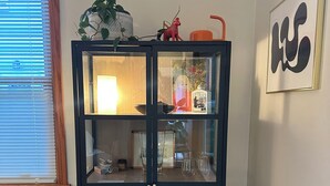 Un meuble aux façades en verre bleu foncé, doté de plusieurs étagères, une petite table avec une lampe et un radiateur posé sur le sol.