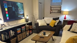Un salon avec un téléviseur à écran plat diffusant une série Netflix, un canapé, une table basse et une bibliothèque.