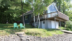 A house with a wooden deck and a stone pathway leading to two green chairs.