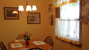 A dining area with a round table, chairs, a chandelier, framed pictures, and a window with curtains.