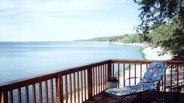 A wooden deck with a view of a lake and a beach.