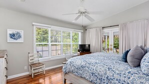 A bedroom with a bed, a chair, a TV, and a window with blinds.