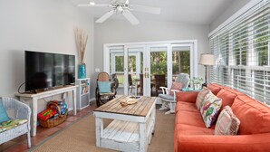 A living room with a TV, wicker chairs, a wooden coffee table, and a red sofa.