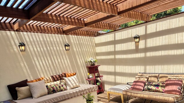 Een zonnig terras met houten afwerking, comfortabele zitplaatsen en een tafeltje met een plant.