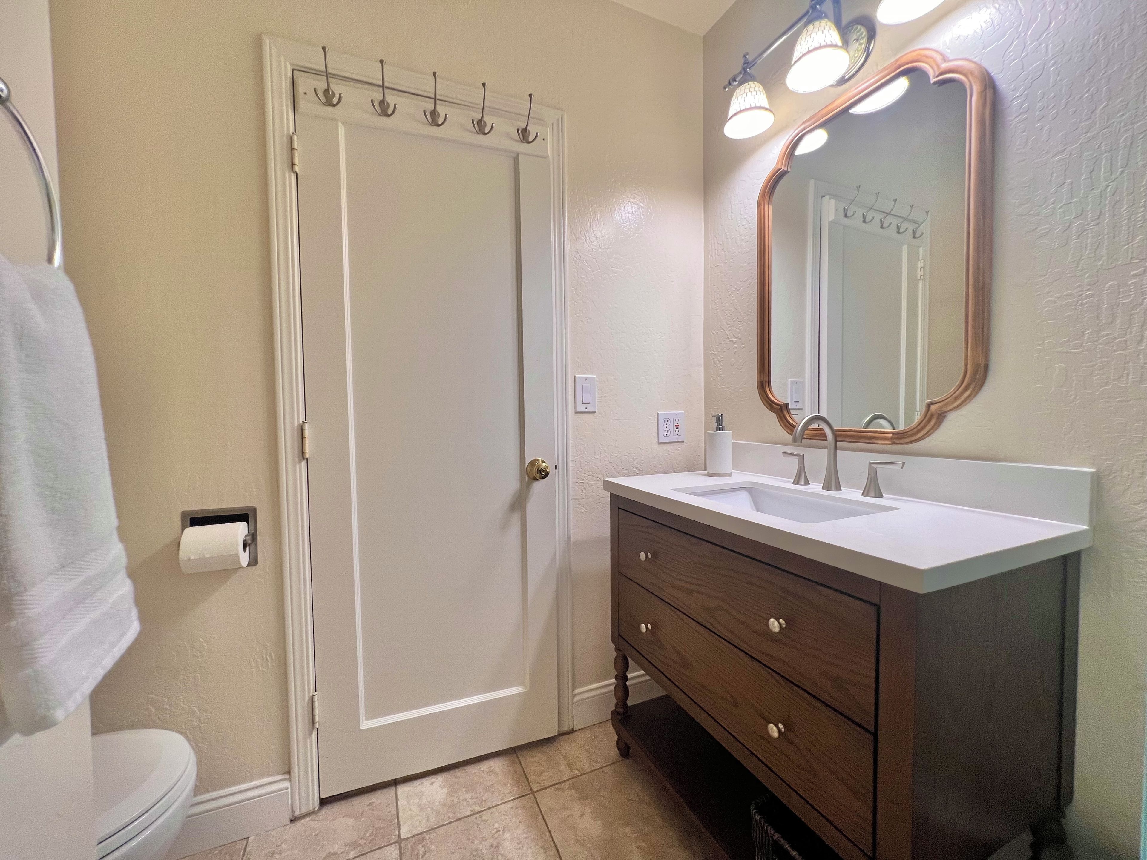A bathroom with a white toilet, a wooden vanity with a mirror, and a towel hanging on the wall.