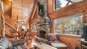 A cozy cabin interior with a stone fireplace, wooden furniture, and a large window with blinds.