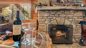 A stone fireplace with a fire, a bottle of wine, and two glasses on a glass table.