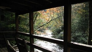A wooden deck with chairs overlooking a forested area and a stream. - Waterfront Cabin on Trout Stream W/ Hot Tub, & Internet (BLUE RIDGE)