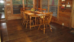 A wooden dining room with a table and chairs, large windows with blinds, and a chandelier. - Waterfront Cabin on Trout Stream W/ Hot Tub, & Internet (BLUE RIDGE)