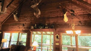 A rustic interior with wooden beams, a chandelier, and deer antlers mounted on the ceiling. - Waterfront Cabin on Trout Stream W/ Hot Tub, & Internet (BLUE RIDGE)