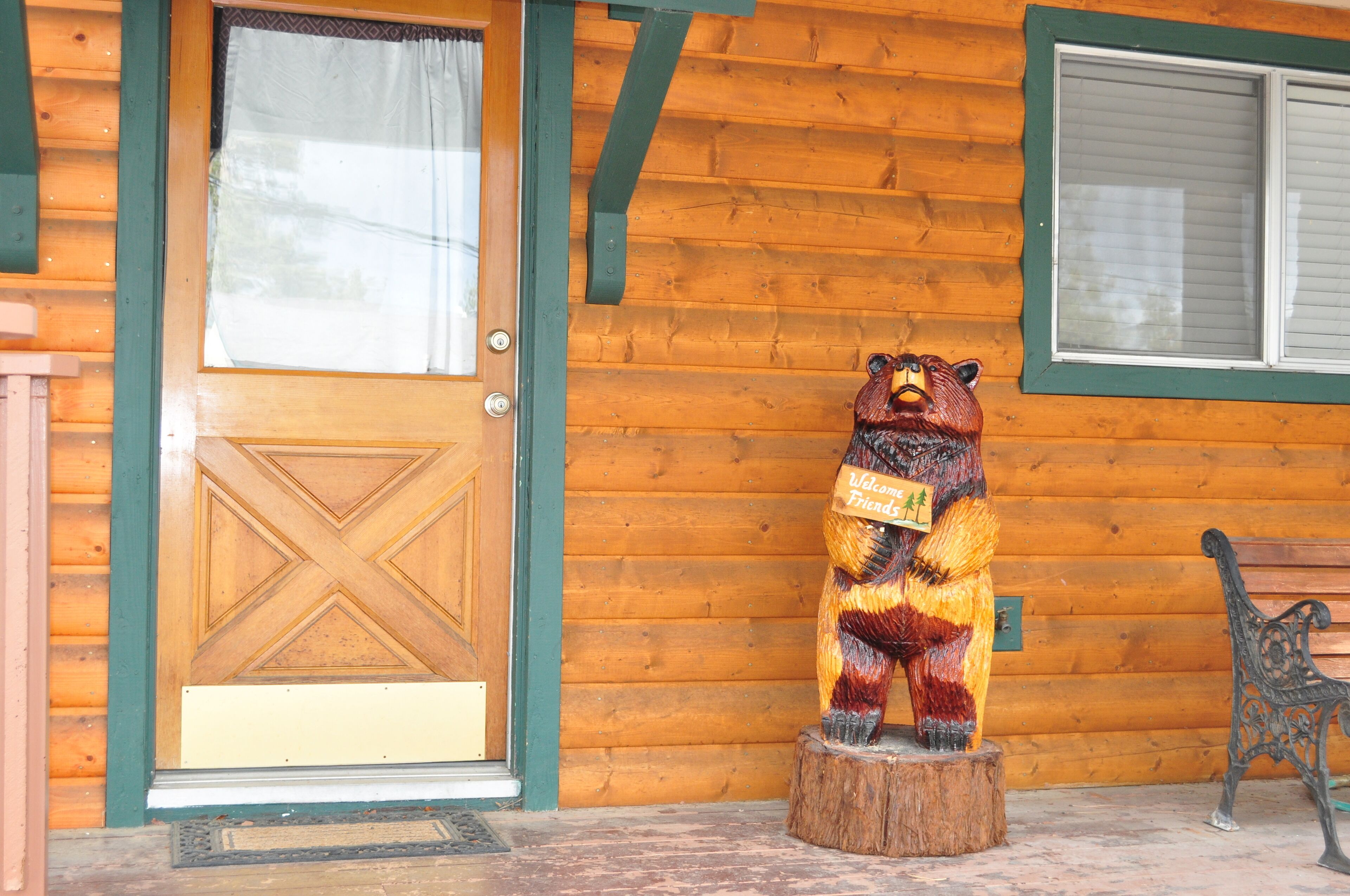 Una cabaña de madera con una estatua de oso sosteniendo un cartel, una puerta y un banco.