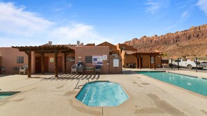 Un espace piscine avec un jacuzzi, un coin salon couvert et un bâtiment doté d’une enseigne.