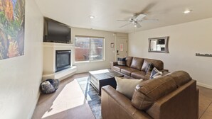 Un salon doté d’une cheminée, d’un ventilateur de plafond, d’un téléviseur et d’une grande fenêtre.