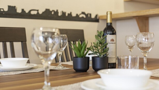 Une table à manger avec des verres à vin, une bouteille de vin et de petites plantes en pot.