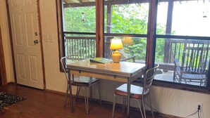 Une pièce dotée d’un plancher en bois, d’une table avec des chaises, d’une lampe et offrant une vue sur l’extérieur grâce à de grandes fenêtres.