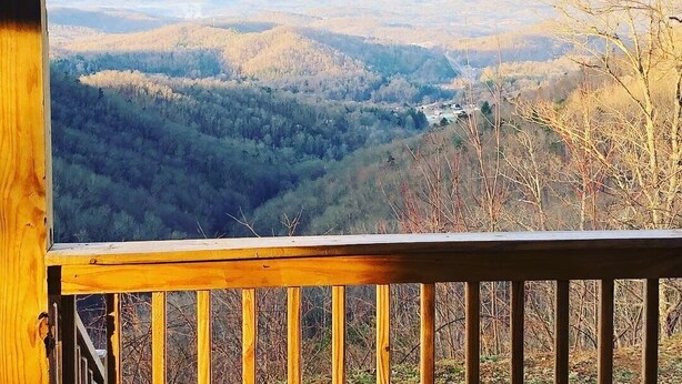 Une vue depuis un balcon en bois donnant sur une vallée, avec des montagnes à l’horizon.