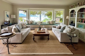 A living room with two sofas, a coffee table, a side table, a bookshelf, and a window with a view. - Oceanfront Home with Spectacular Views (Salt Spring Island)