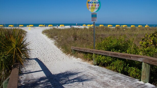 A beach access sign at 68th Ave with beach access restrictions and a wooden boardwalk leading to the beach.