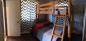 Una cama litera con escalera de madera, una colcha roja y una cortina con estampado en chevron.