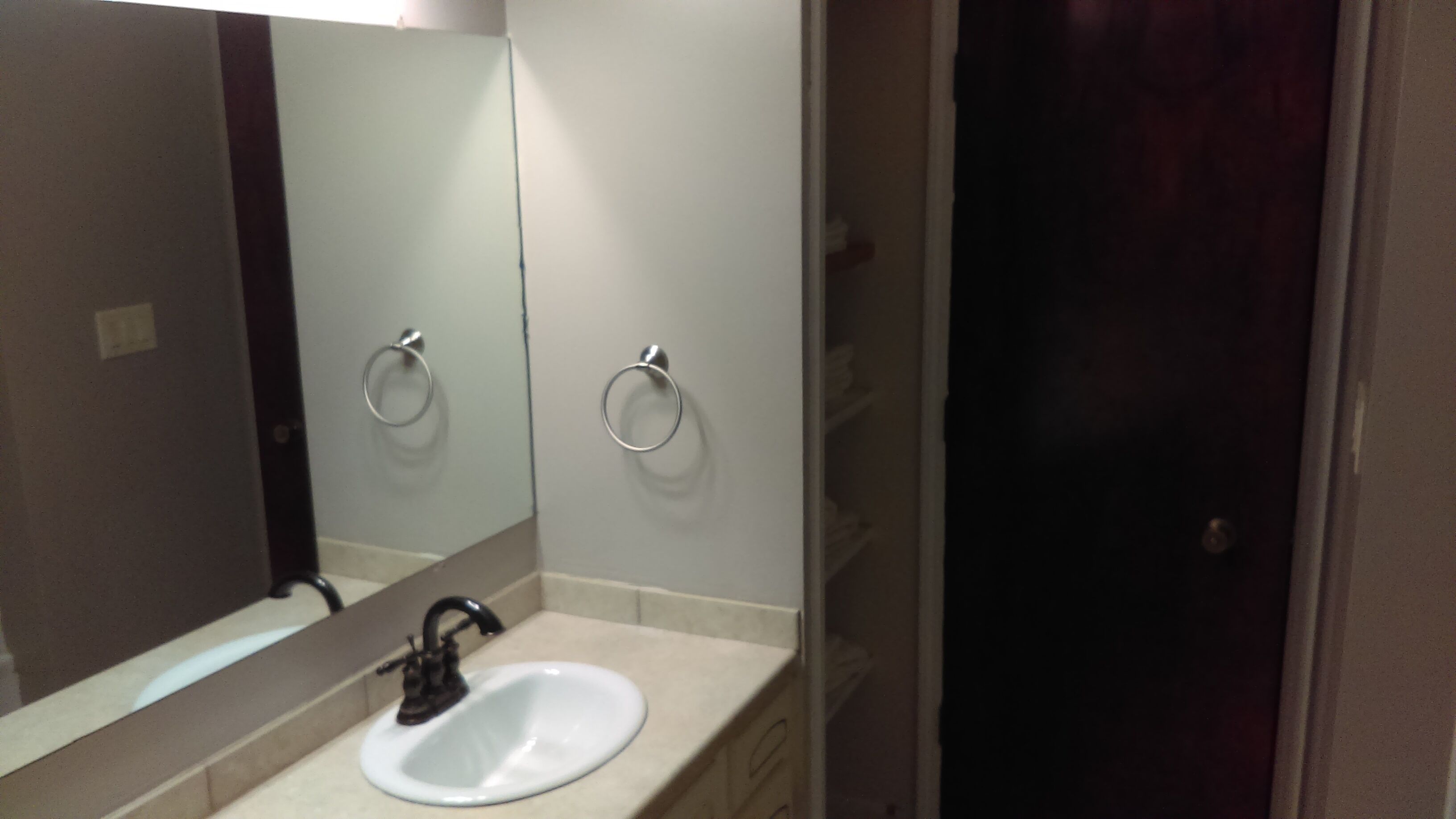Un baño con un lavamanos blanco, un espejo y dos anillas para toallas en la pared.