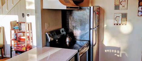 A kitchen with wooden cabinets, a stainless steel refrigerator, and a stove. There is a countertop with a coffee machine and a kettle.