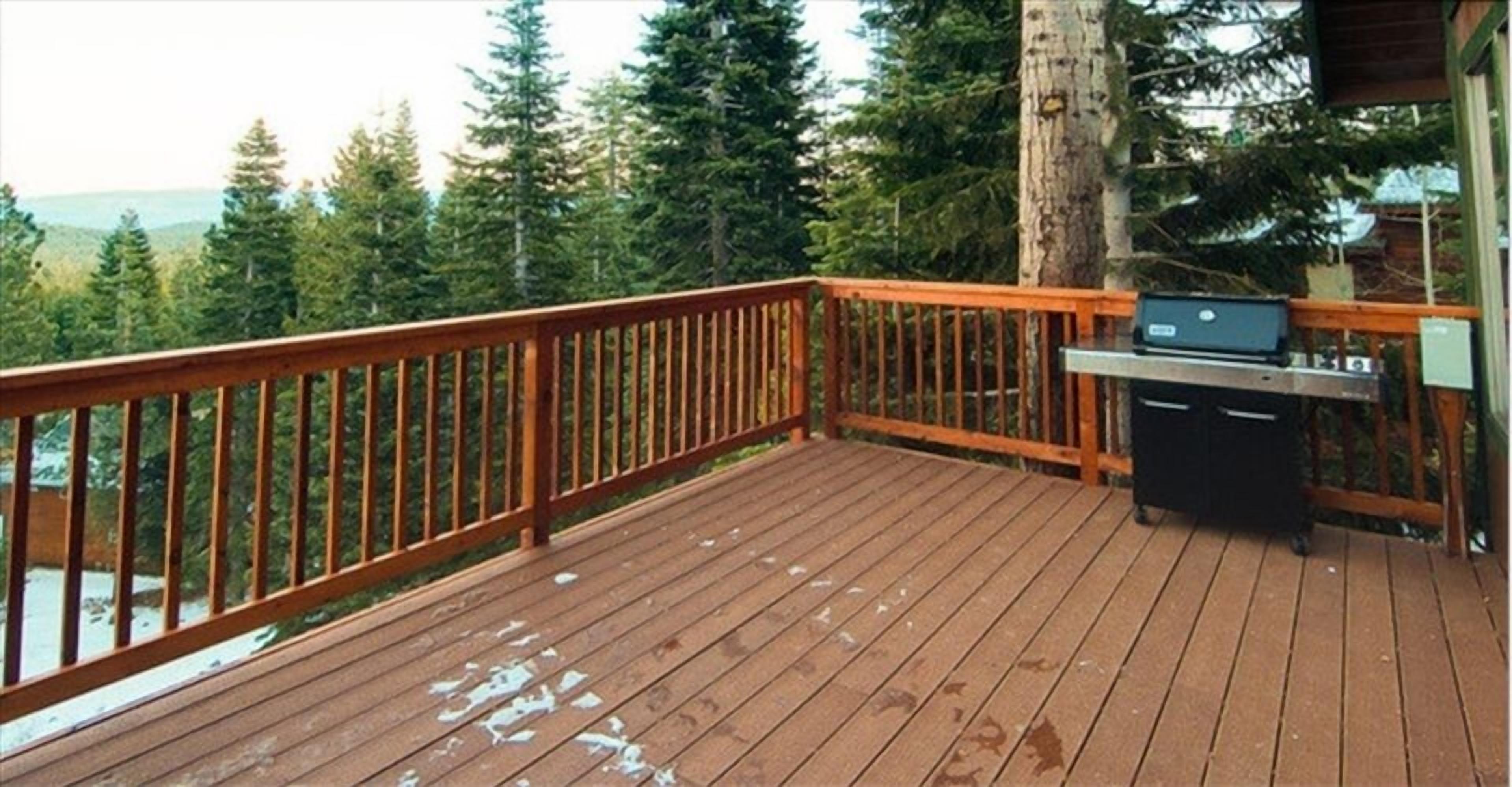 A wooden deck with a grill and a laptop, surrounded by trees and a view of the mountains.