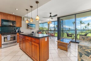 A modern kitchen with wooden cabinets, a central island, and a dining area with chairs and a table. - 312 - Fantastic remodeled oceanfront with great ocean view and A/C! (Kihei)