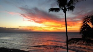Un coucher de soleil sur l’océan, avec des palmiers se découpant en silhouette sur le ciel.