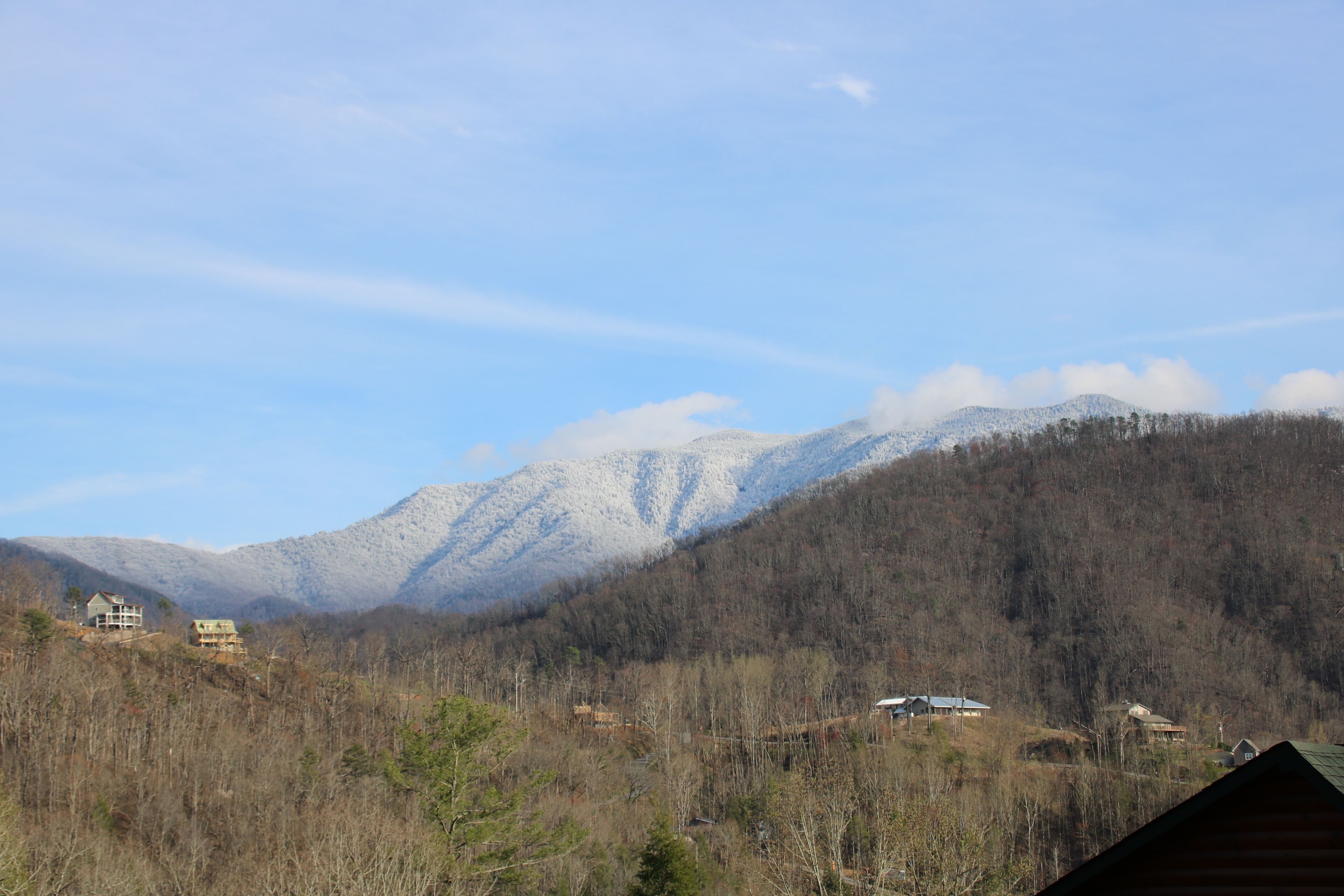 Un paisaje montañoso con varias construcciones, incluyendo casas y una cabaña, rodeado de árboles y picos nevados.