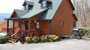 Eine Blockhütte mit Veranda, zwei Fenstern und einem Grill vor der Tür.