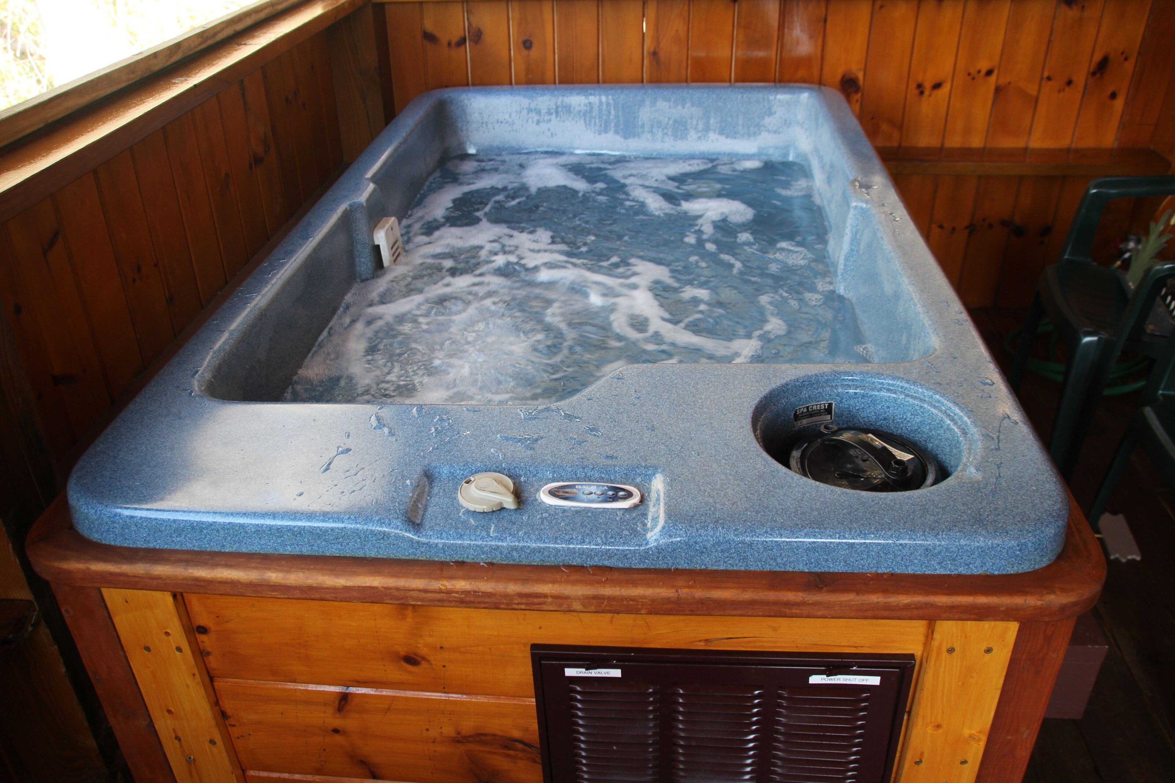 A wooden hot tub with a blue interior, a drain, and a control panel.