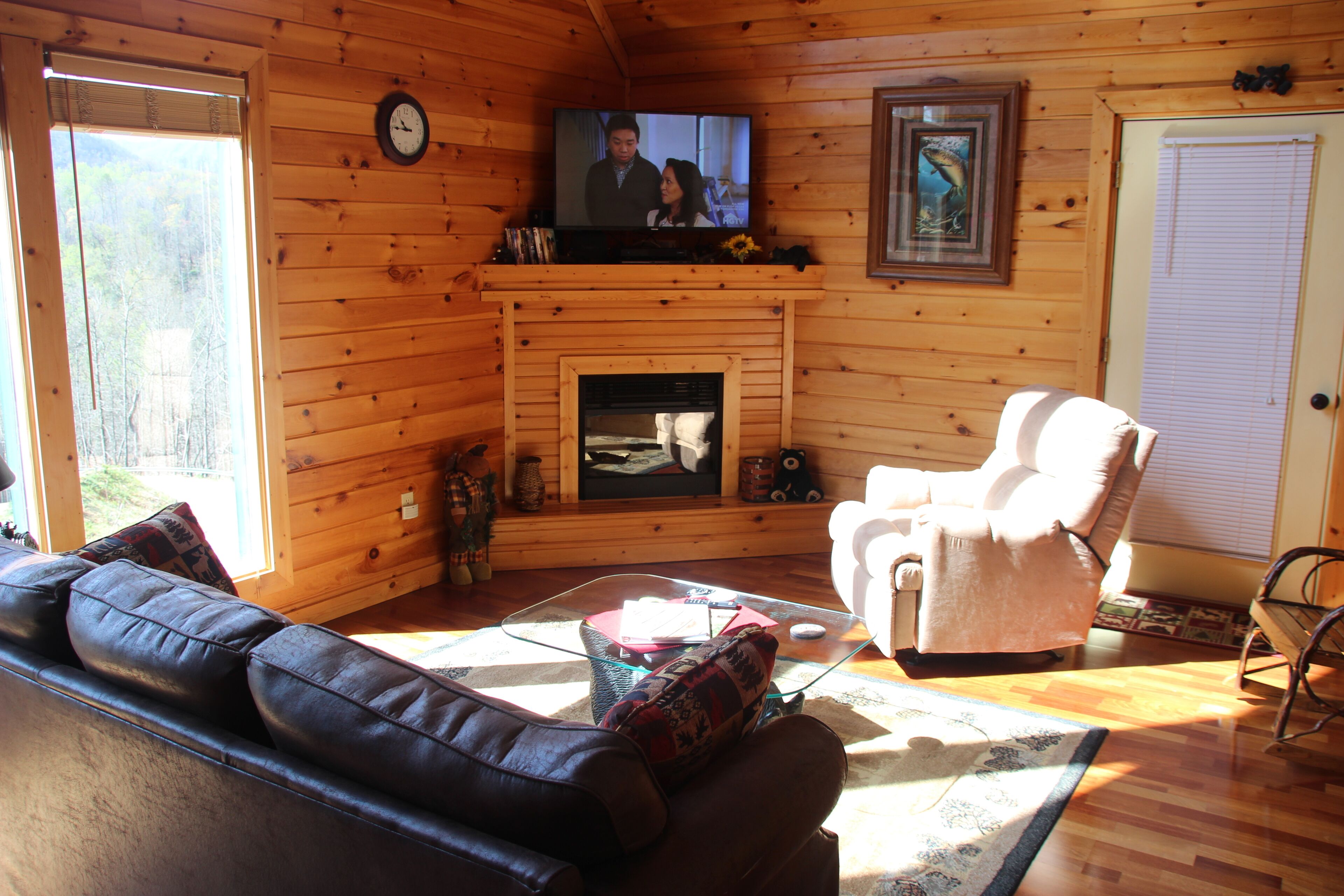 Interior acogedor de una cabaña con chimenea, sofá de cuero y televisor montado encima.