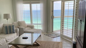 A spacious living room with a glass coffee table, a sofa, and a chair. There is a ceiling fan, a lamp, and a view of the ocean through large windows. - Guests Rate Us Exceptional: Beach chairs  & umbrellas available for rent. (Pensacola Beach)