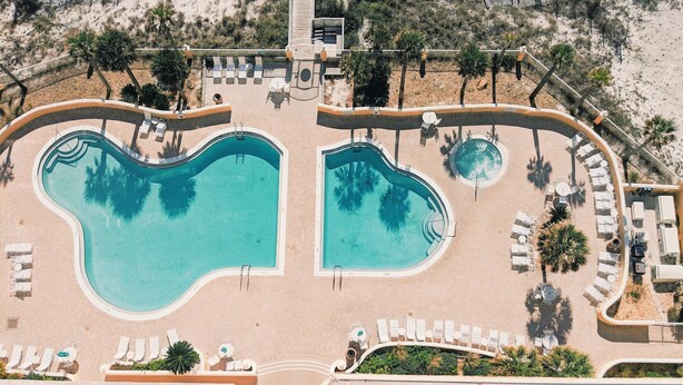 A resort with two large swimming pools, sun loungers, and a beach area. - Guests Rate Us Exceptional: Beach chairs  & umbrellas available for rent. (Pensacola Beach)