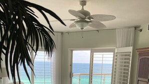 A living room with a view of the ocean, a ceiling fan, and a large plant. - Guests Rate Us Exceptional: Beach chairs  & umbrellas available for rent. (Pensacola Beach)