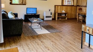 Een woonkamer met een houten plafond, een televisie, een bank, een salontafel en een eethoek met een tafel en stoelen.