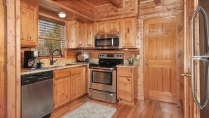 A compact kitchen with wooden cabinets, a microwave, a stove, and a dishwasher. - Misty Mornings: Rustic Resort Cabin - Pet Friendly - New Hot Tub (Sevierville)
