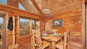 A wooden cabin interior with a dining table, chairs, and a painting on the wall. - Misty Mornings: Rustic Resort Cabin - Pet Friendly - New Hot Tub (Sevierville)